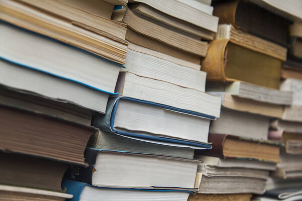 Vintage paper books lie uneven piles behind glass on a show-window of secondhand bookshop