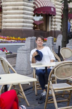 Moskova, Rusya, üzerinde 10 Ağustos 2017. Cafe tarihsel Dükkanı bilinen alışveriş merkezi olan sakız arka planı küçük bir masa ve bir Moskova sembollerin genç çekici kadın mavi bir şapka ile oturur. 