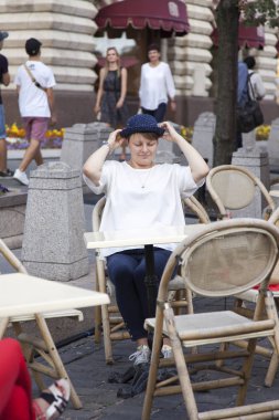 Moskova, Rusya, üzerinde 10 Ağustos 2017. Cafe tarihsel Dükkanı bilinen alışveriş merkezi olan sakız arka planı küçük bir masa ve bir Moskova sembollerin genç çekici kadın mavi bir şapka ile oturur. 