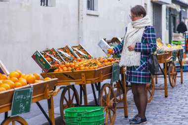 Paris, Fransa, 1 Kasım 2017. Çeşitli sebze ve meyve Muftard Caddesi'ndeki geleneksel çiftçi pazarının bir gösteri penceresinde yerleştirilir. Genç çekici kadın portakal seçer