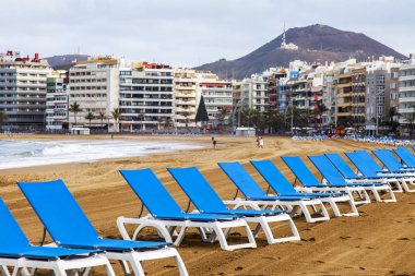 Las Palmas de Gran Canaria, İspanya, 6 Ocak 2018 üzerinde. Waterfront mesafe ve Atlantik okyanus kıyısında Playa de Las Canteras plaj kış bilir. Mavi şezlong tatilcilerin için bekleyin