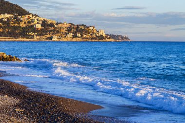 Güzel, Fransa, 6 Mart 2018. Günbatımı güneş dağ onun kıyısında dalgalar deniz sörf pitoresk bir koyda ve Bina Işıkları