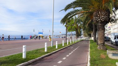 Güzel, Fransa, 9 Ekim 2019. Ünlü Promenade des Anglais seti ve deniz kıyısındaki şehir plajı. Palmiye ağaçlarının altında bisiklet izi