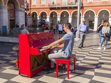 Güzel, Fransa, 9 Ekim 2019. Adam kırmızı piyano çalıyor ve şehrin merkez meydanından geçenleri eğlendiriyor - Place Massena