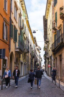 Verona, İtalya, 24 Nisan 2019 tarihinde. İnsanlar eski şehirde dar pitoresk sokak boyunca gitmek