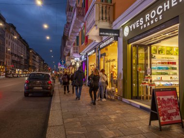 Milan, İtalya, 12 Şubat 2020. Şehir merkezindeki alışveriş caddesinde akşam aydınlığında. Çok sayıda mağazanın vitrinleri zarif vitrinlerle alıcıları cezbediyor