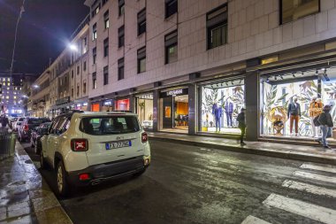 Milan, İtalya, 12 Şubat 2020. Şehir merkezindeki alışveriş caddesinde akşam aydınlığında. Çok sayıda mağazanın vitrinleri zarif vitrinlerle alıcıları cezbediyor