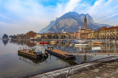 Lecco, İtalya, 16 Şubat 2020. Como Gölü 'nün bulutlu havadaki manzaralı seti ve arkasındaki dağlar. Tekneler suya yansır.