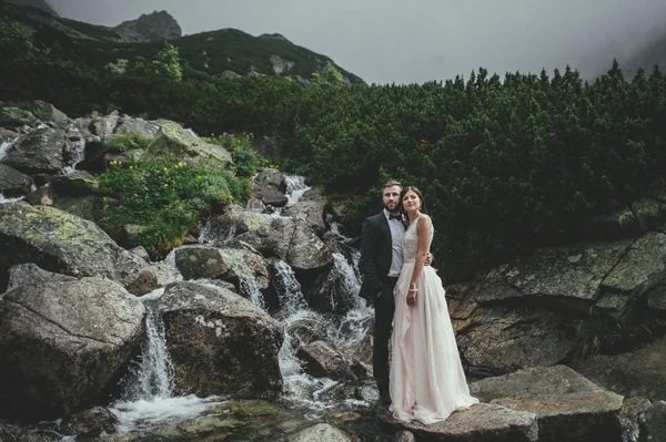 Recém-casados abraçando perto de cachoeira fria — Fotografia de Stock