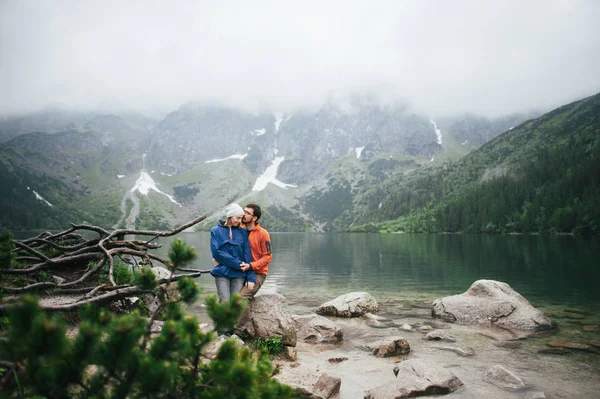 Casal de viajantes em pé na rocha perto do lago — Fotografia de Stock