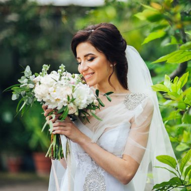 Zarif beyaz elbiseli buket tutarak ve parkta poz güzel gelin