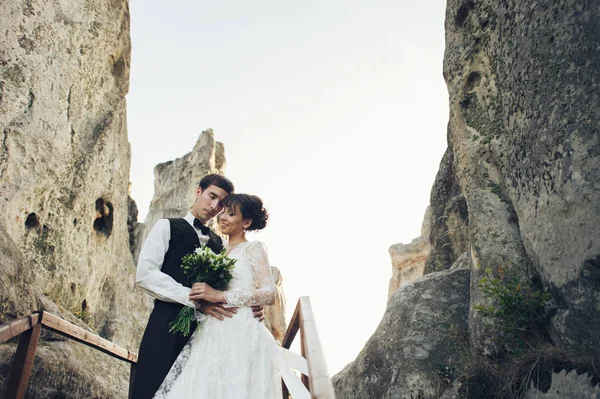 beautiful caucasian engaged couple with flowers bouquet hugging in rocky park