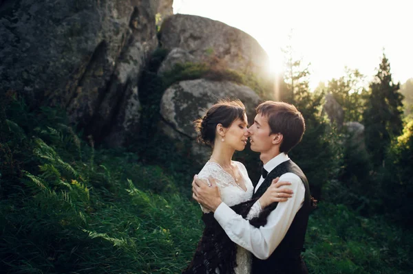 young attractive caucasian engaged couple hugging besdie rocks at park