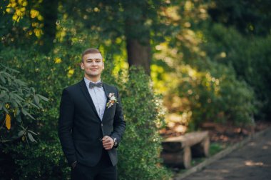 Genç şık damat park yeşil ağaçların karşı poz