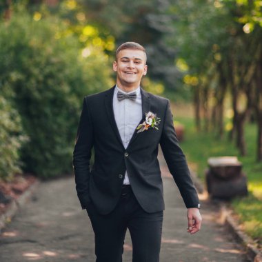 Genç şık damat park yeşil ağaçların karşı poz