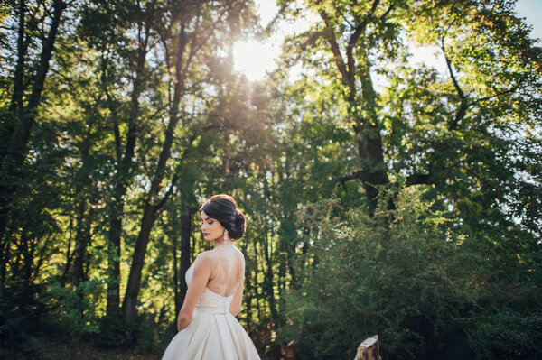 Back view of stylish young bride against green trees