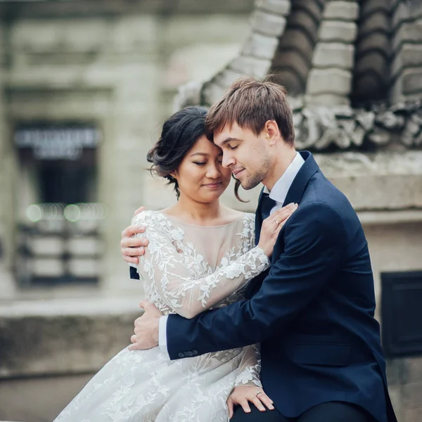 Bride with groom sitting on fountain with statue of Poseidon