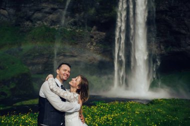 Evli çift gökkuşağı ile şelale yakınındaki sarılma 