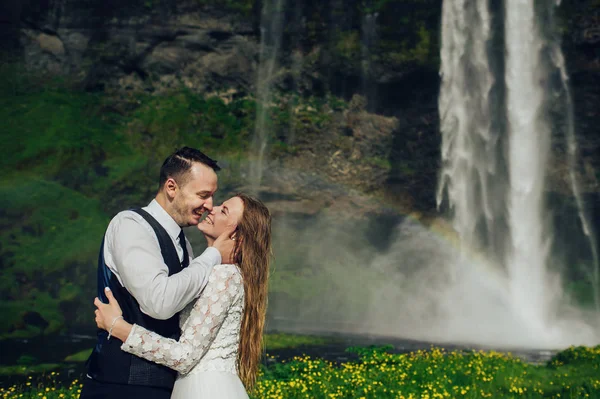 新婚夫妇抱着彩虹靠近瀑布 — 图库照片