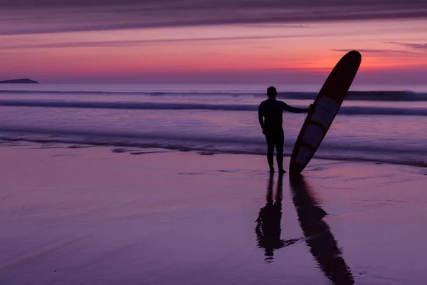 Surfista em pé na praia ao pôr do sol — Fotografia de Stock