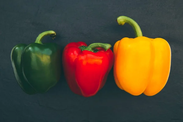 Red yellow green bell peppers overhead on dark background
