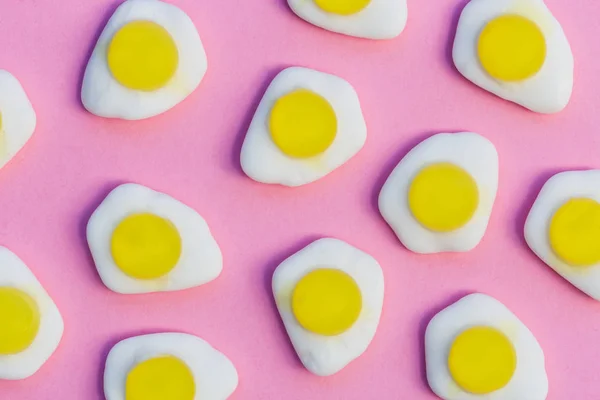 Fried eggs candy sweets overhead on bright pink background