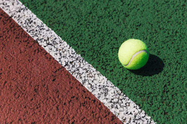 Yellow tennis ball on green tennis court line