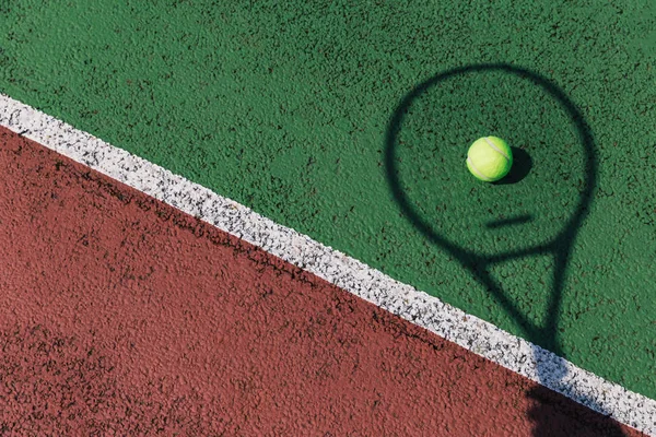 Tennis racket shadow and ball on green tennis court