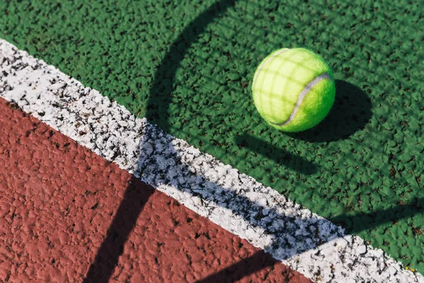 Tennis racket shadow and ball on green tennis court