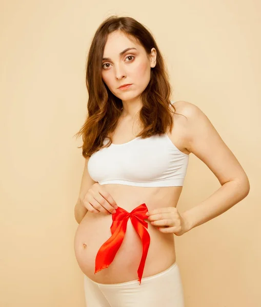 Zwangere vrouw met rood lint op haar buik — Stockfoto