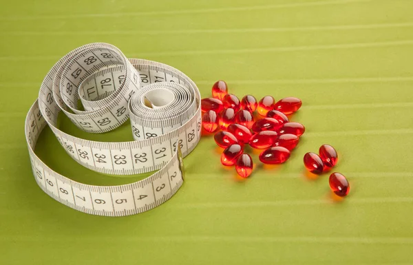 Pilules et ruban à mesurer sur fond vert — Photo