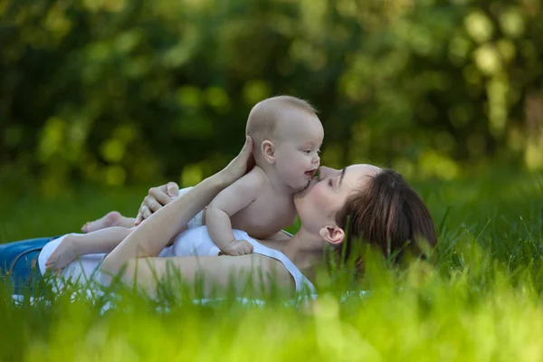 Жінка тримає в руці дитину в саду і лежить на траві — стокове фото