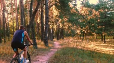 Bisikletli adam orman yolunda gidiyor.