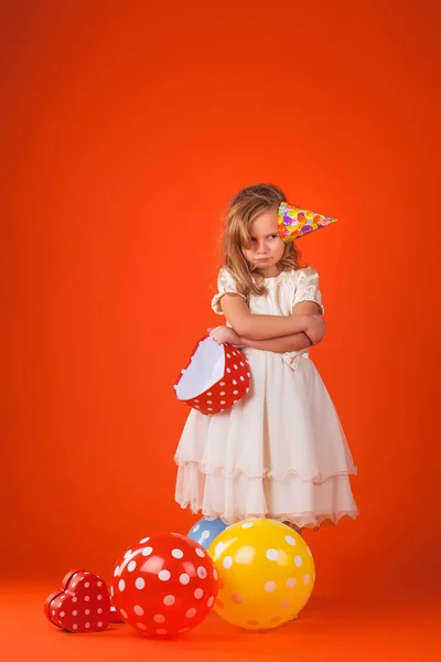 Turuncu arka planda hediyeleri ve balonları olan bir kız.. — Stok fotoğraf