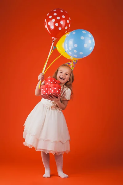 Chica con regalos y globos sobre un fondo naranja . — Foto de Stock