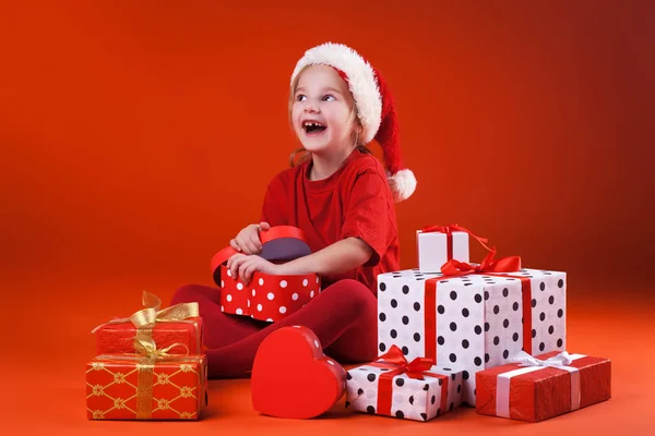 Cute girl in santa claus hat opens christmas presents — Stock Photo, Image