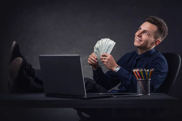 Masadaki başarılı iş adamı karanlık bir arkaplanda dizüstü bilgisayar ve parayla. — Stok fotoğraf