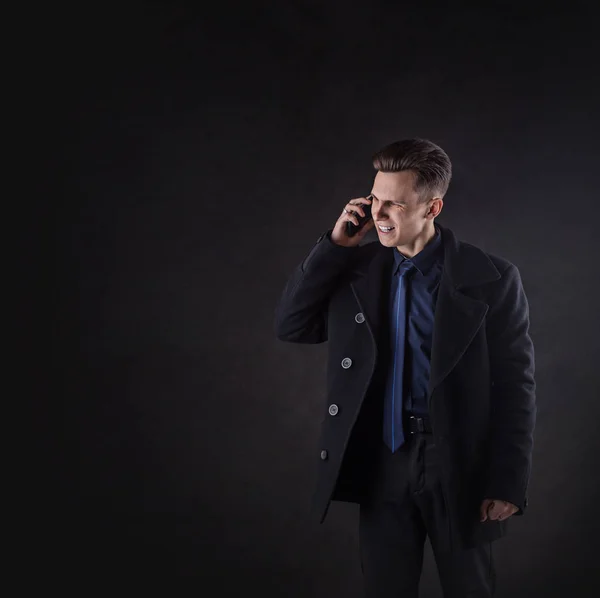 A handsome man in a coat screams while talking on the phone. — Stock Photo, Image