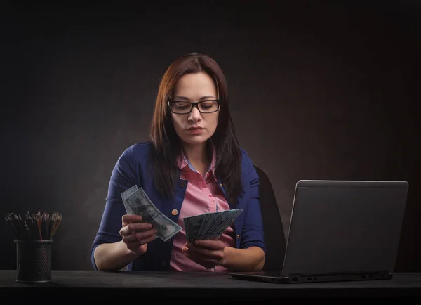 Successful businesswoman at the table on a dark background with laptop and money. — Stock Photo, Image