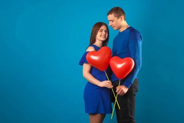 Junges verliebtes Paar auf blauem Hintergrund mit roten Luftballons. — Stockfoto