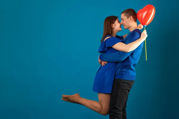 Jovem casal apaixonado em um fundo azul com balões vermelhos . — Fotografia de Stock