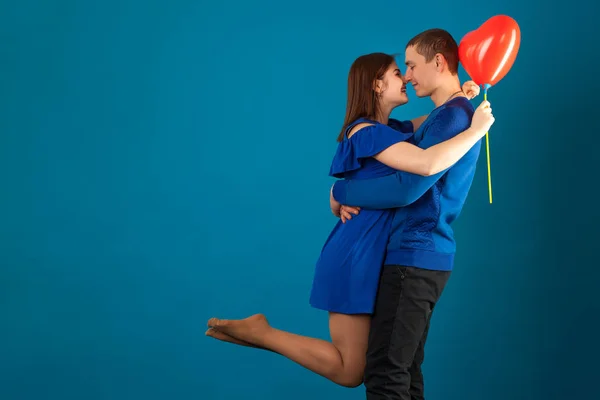 Junges verliebtes Paar auf blauem Hintergrund mit roten Luftballons. — Stockfoto