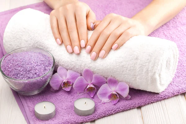 Hermosa manicura rosa con orquídea, vela y toalla en la mesa de madera blanca . — Foto de Stock