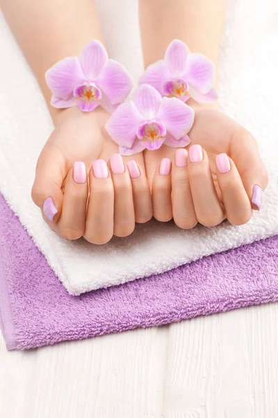 Hermosa manicura rosa con orquídea, y toalla en la mesa de madera blanca . —  Fotos de Stock