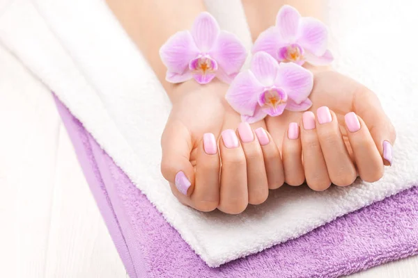 Beautiful pink manicure with orchid, and towel on the white wooden table. — 스톡 사진