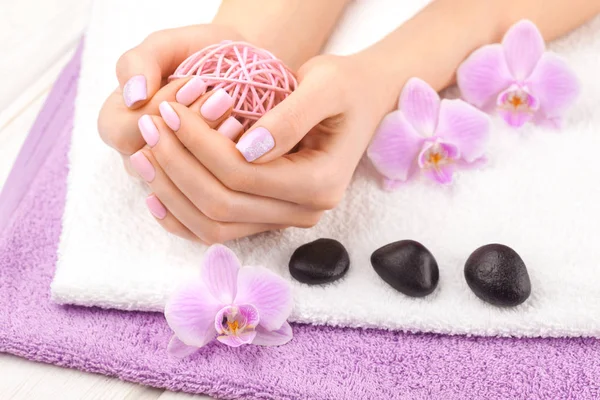 Hermosa manicura rosa con orquídea, y toalla en la mesa de madera blanca . — Foto de Stock