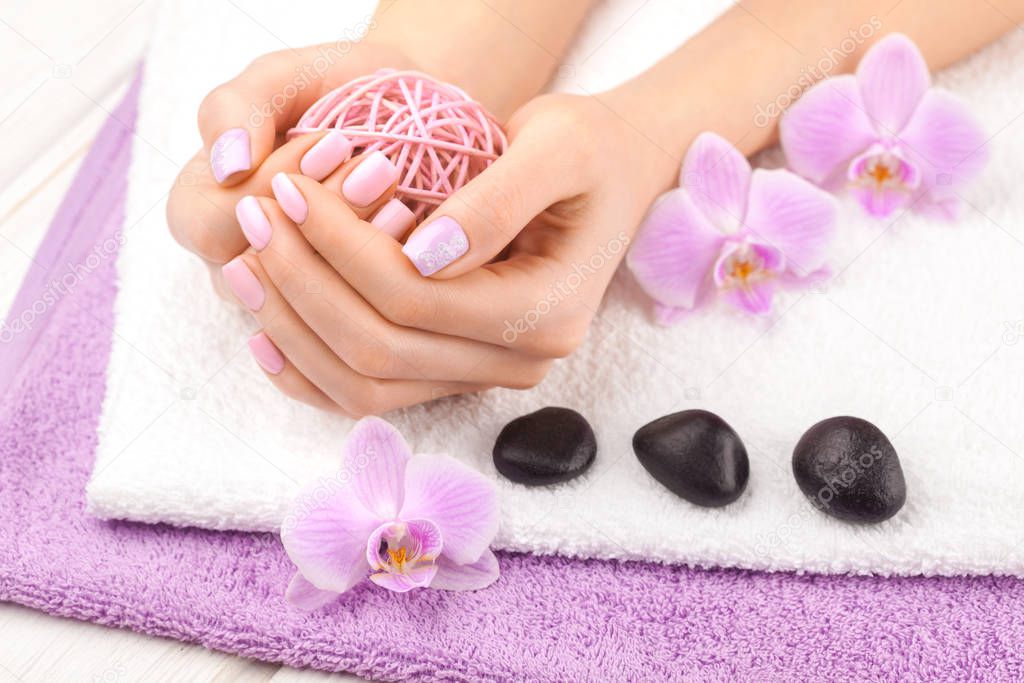 beautiful pink manicure with orchid, and towel on the white wooden table.