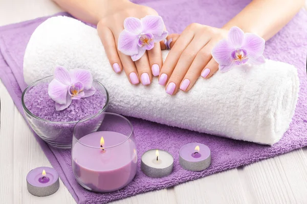 Piękny różowy manicure z orchideą, świeca i ręcznik na białym drewnianym stole. — Zdjęcie stockowe