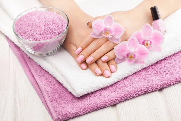 Bella manicure rosa con orchidea, e asciugamano sul tavolo di legno bianco . — Foto Stock