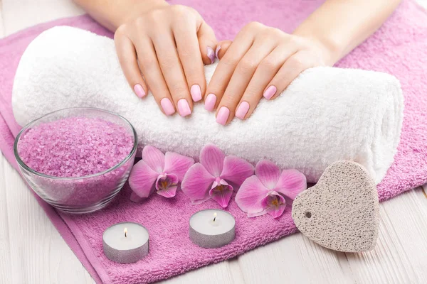 Piękny różowy manicure z orchideą, świeca i ręcznik na białym drewnianym stole. — Zdjęcie stockowe